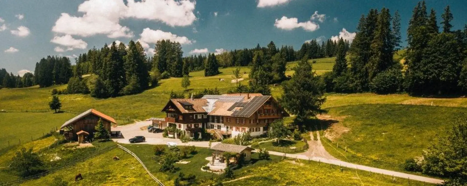 - © https://westenried.de Luftaufnahme eines MirAllgäuer Bauernhofs im Allgäu, umgeben von grünen Wiesen, Bäumen und naturnaher Landschaft. Der Hof liegt idyllisch inmitten der Allgäuer Natur unter blauem Himmel.